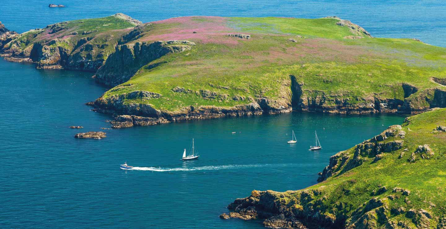 A Boat Is Sailing In The Water Near A Green Island Wallpaper