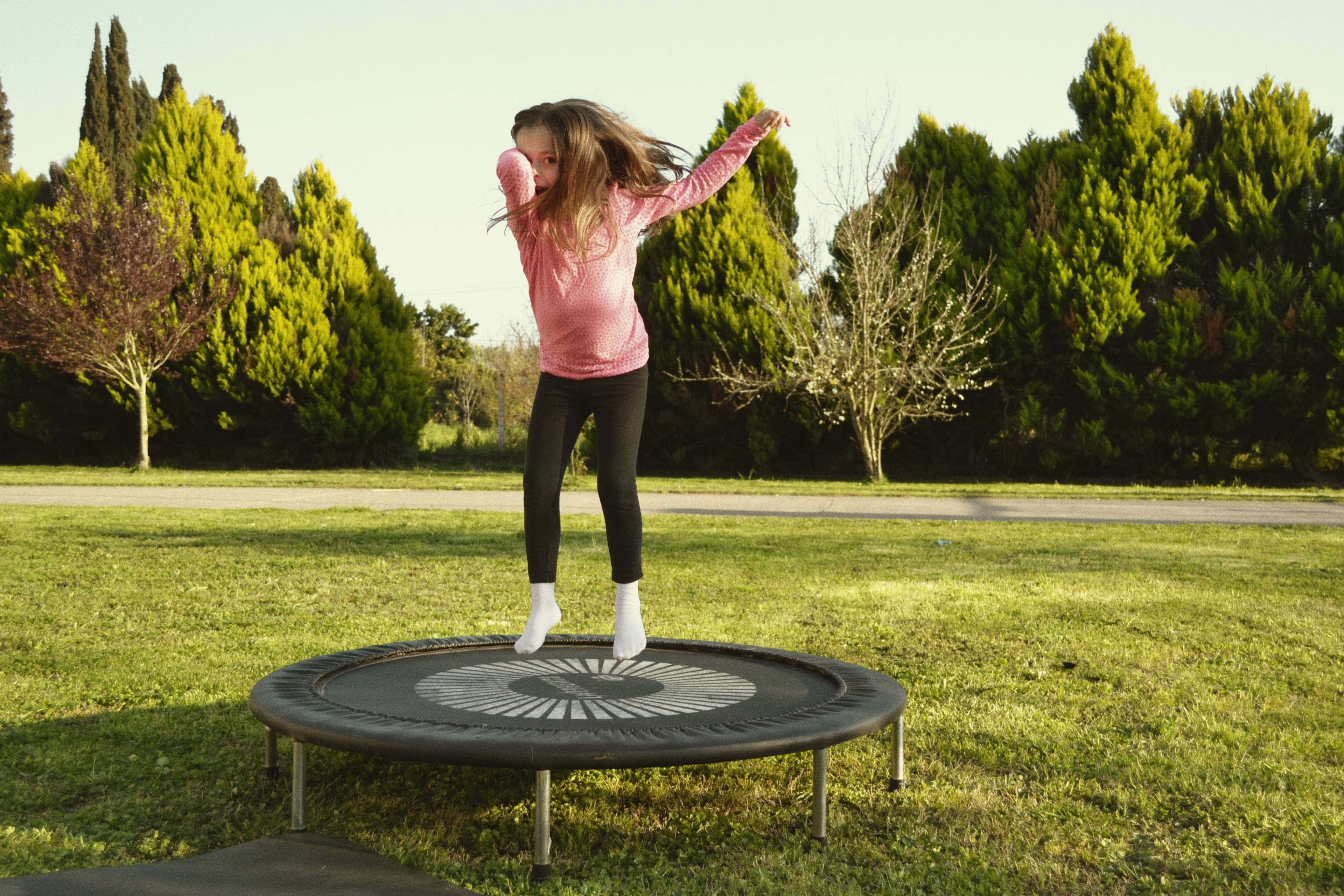 A Child Joyfully Jumping On A Trampoline Under A Bright Sky. Wallpaper