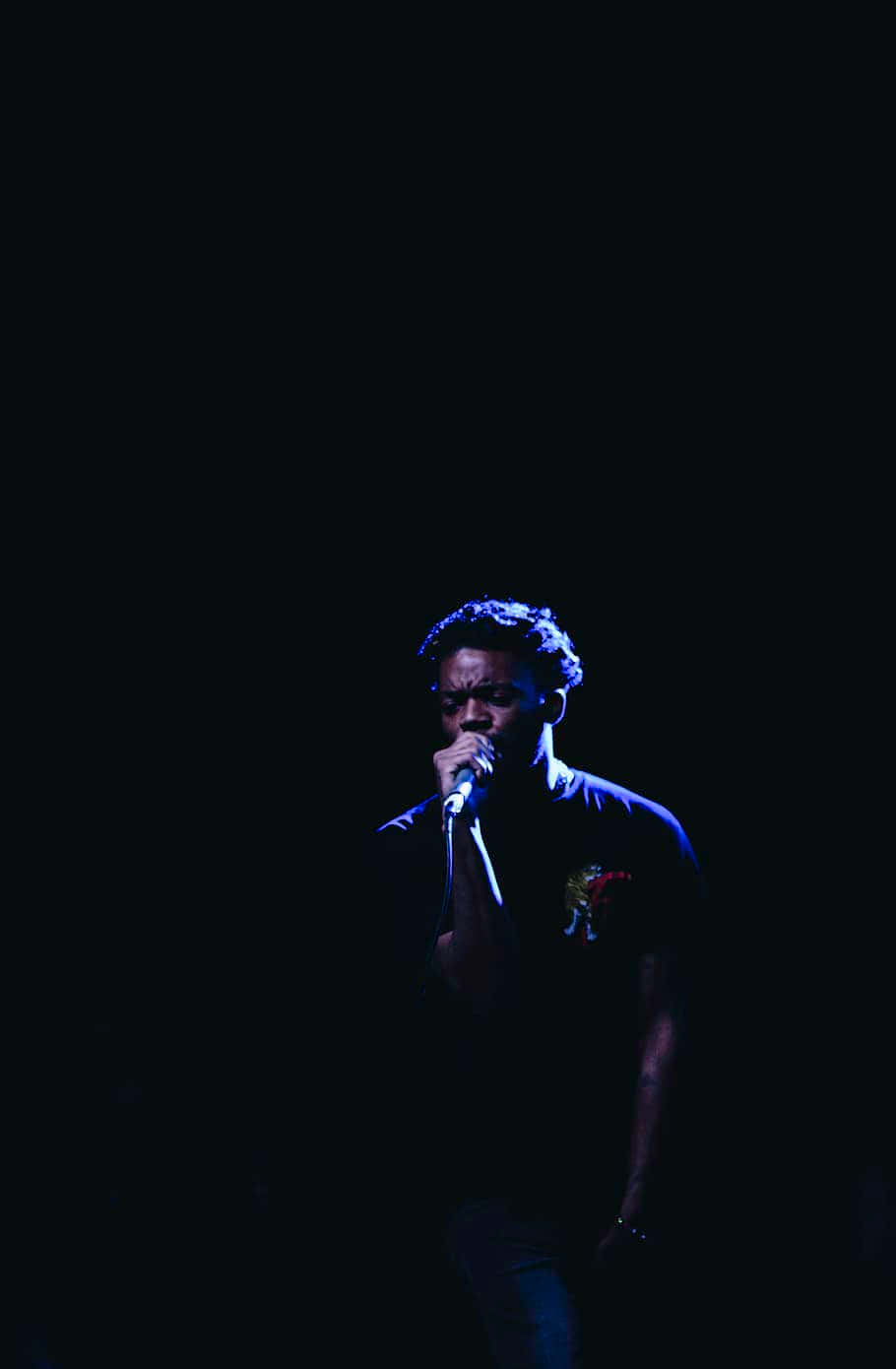 A Man Singing Into A Microphone In The Dark Wallpaper