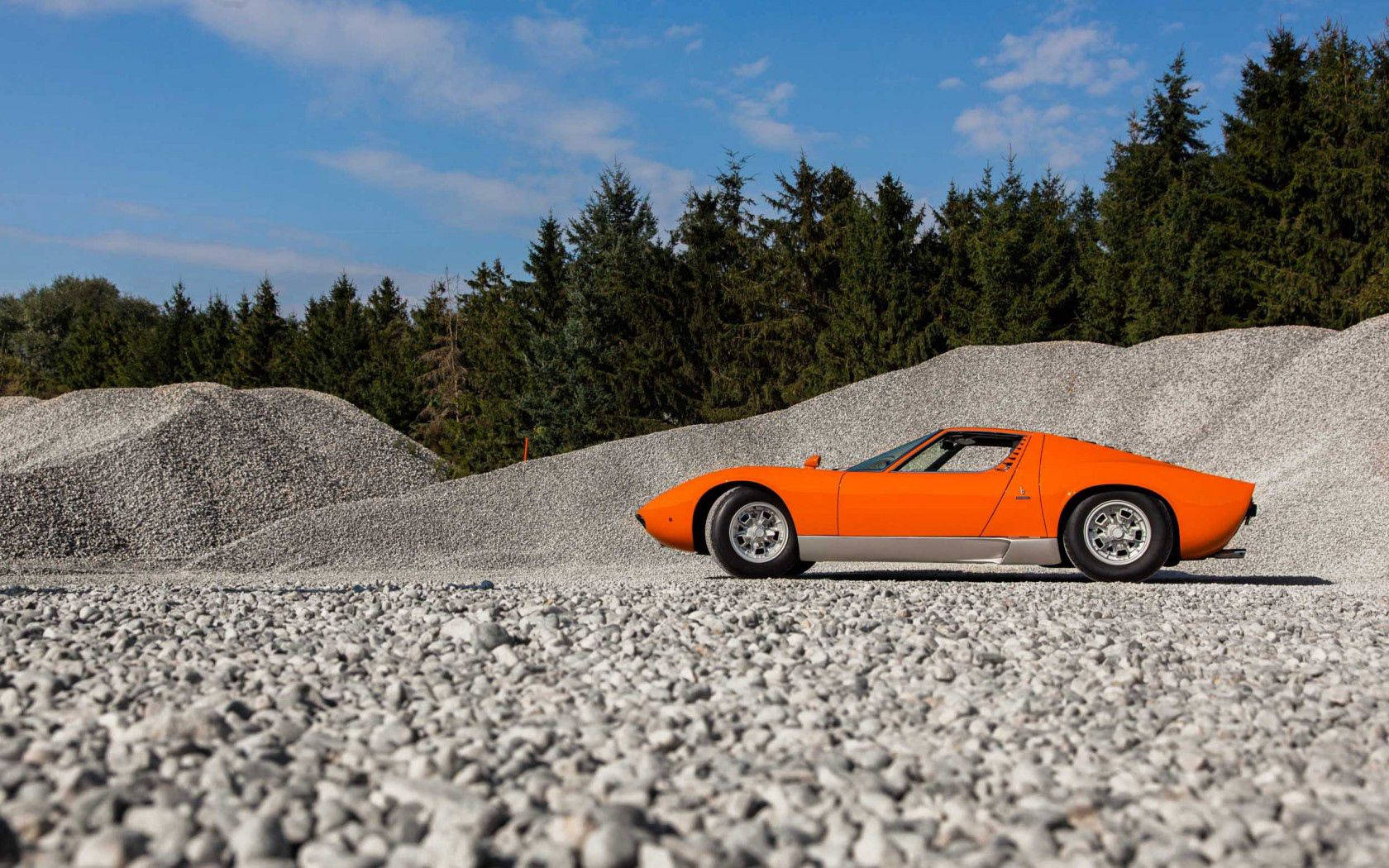 An Exquisite Orange Lamborghini Miura On A Gravel Road. Wallpaper