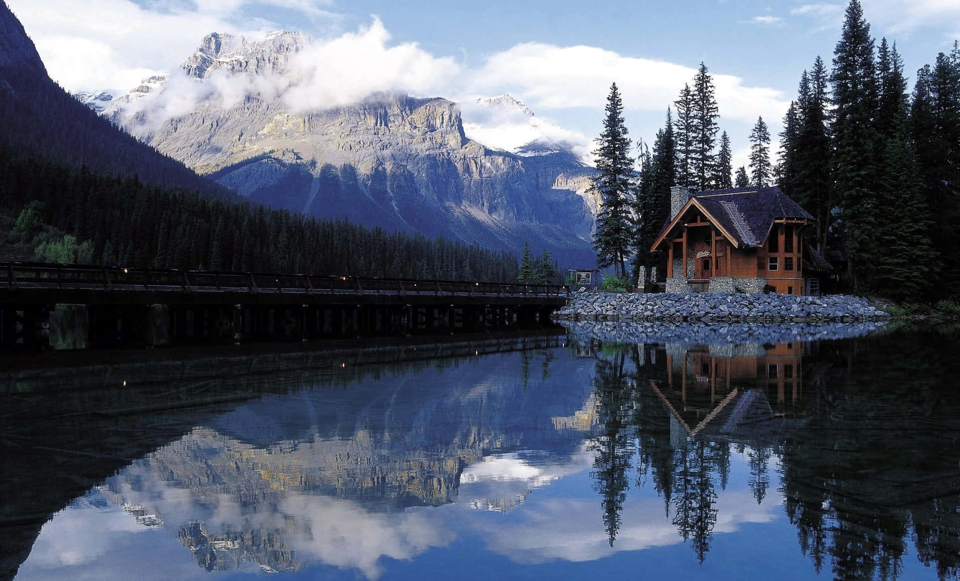 Cabin By A River Surrounded By Mountains And Nature Wallpaper