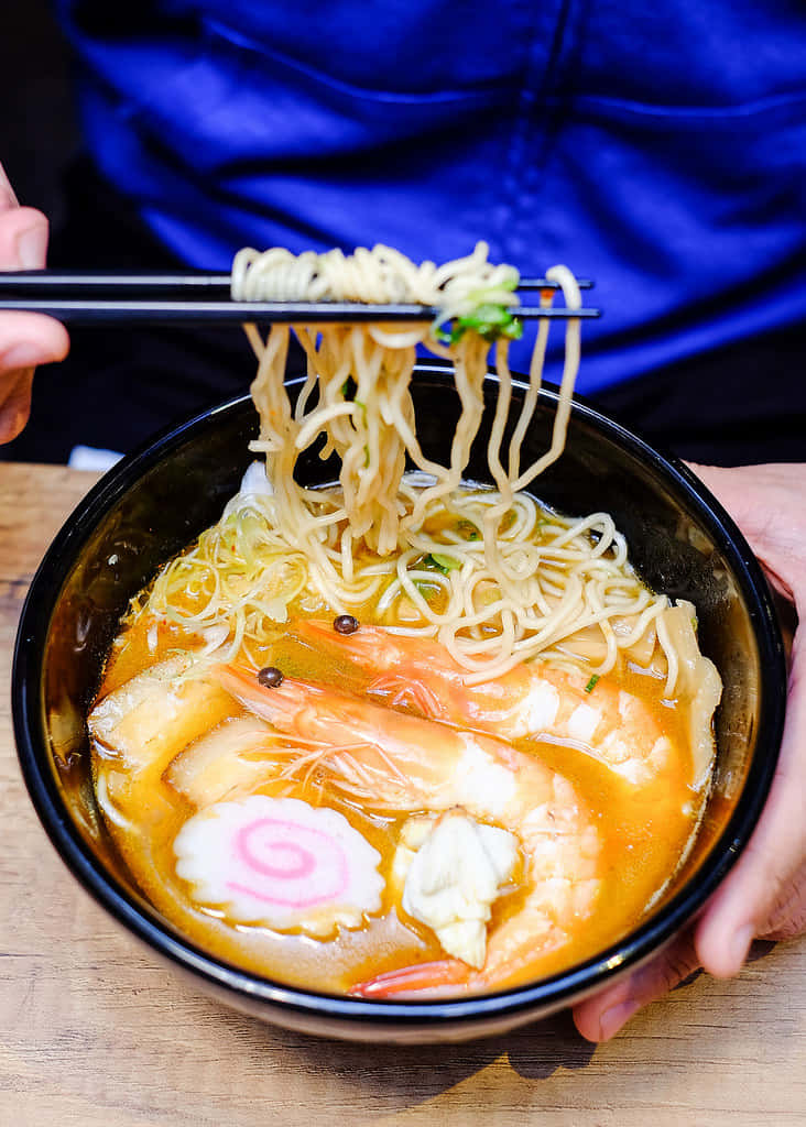 Person's Hand Grabbing Ramen Using Chopsticks Wallpaper