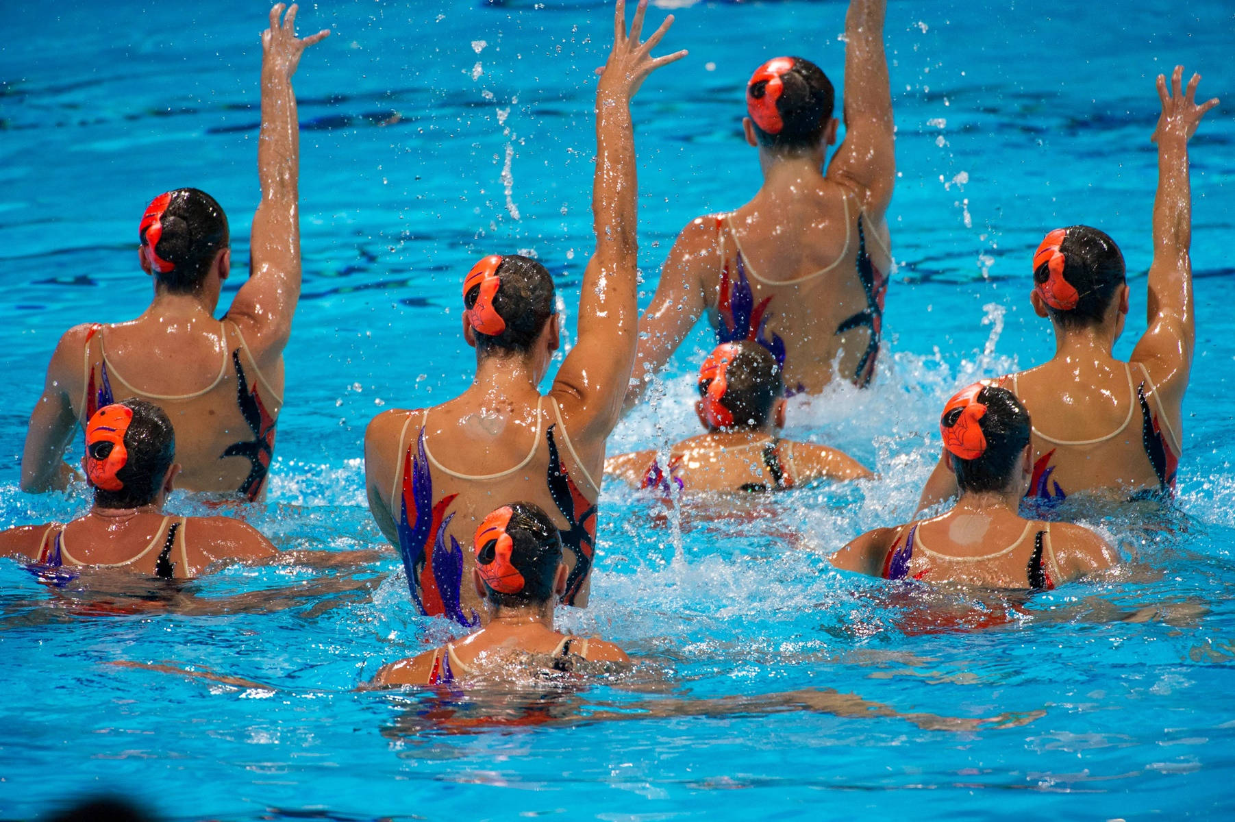 Synchronized Swimmers With Hands Up In Perfect Harmony Wallpaper