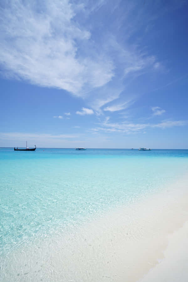 A Beach With Clear Water And A Boat In The Distance Wallpaper