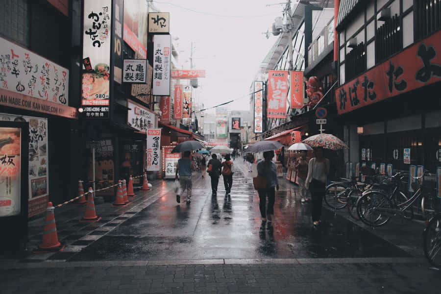 A City Street With People Walking With Umbrellas Wallpaper