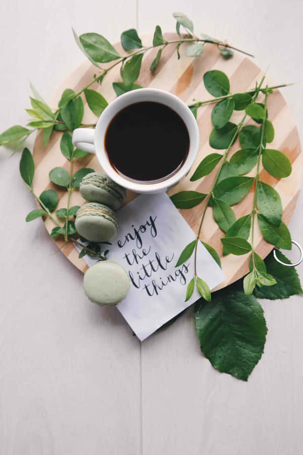 A Cup Of Coffee With Macarons And Greenery On A Wooden Plate Wallpaper