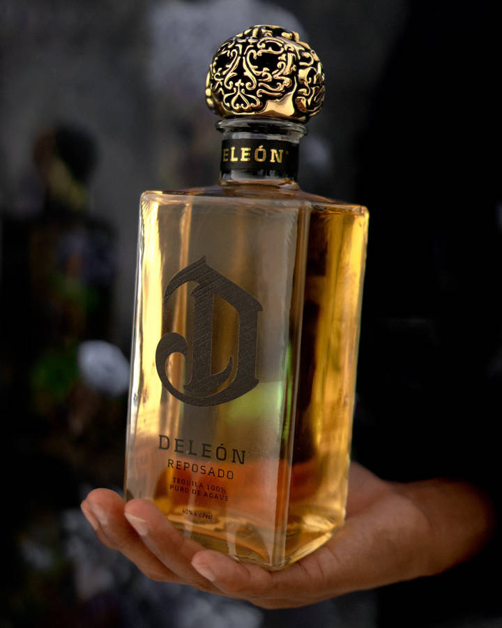 A Hand Holding A Bottle Of Deleon Tequila's Golden Reposado Wallpaper