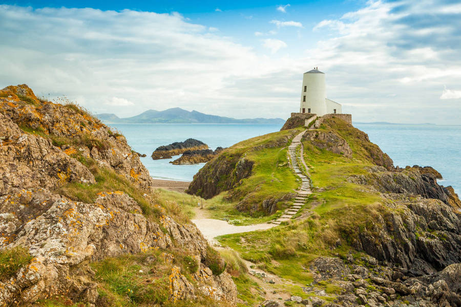 A Lighthouse On A Rocky Cliff Overlooking The Ocean Wallpaper