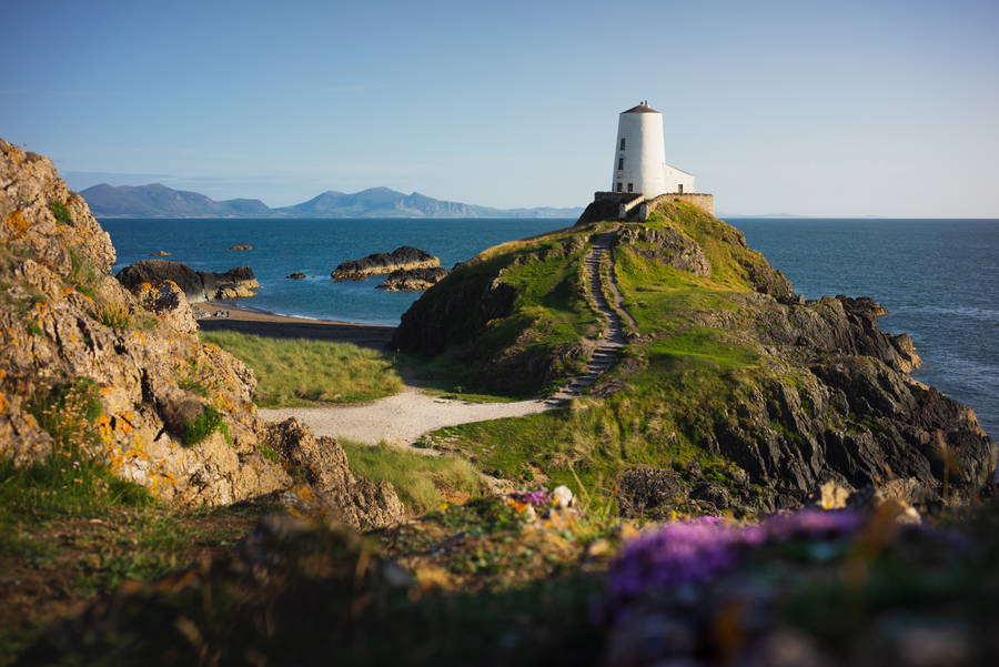 A Lighthouse Sits On Top Of A Rocky Cliff Wallpaper