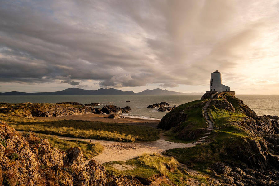 A Lighthouse Sits On Top Of A Rocky Cliff Overlooking The Ocean Wallpaper