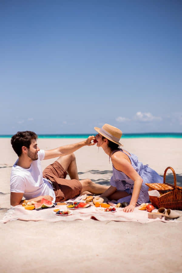 A Loving Moment: Couple Enjoying A Relaxing Picnic On The Beach Wallpaper