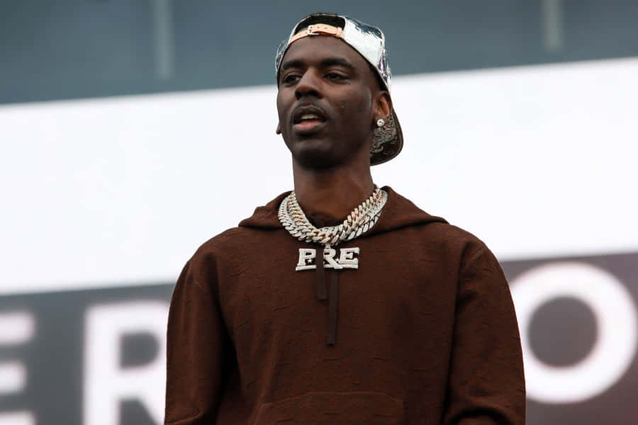 A Man In A Brown Hoodie Is Standing On Stage Wallpaper