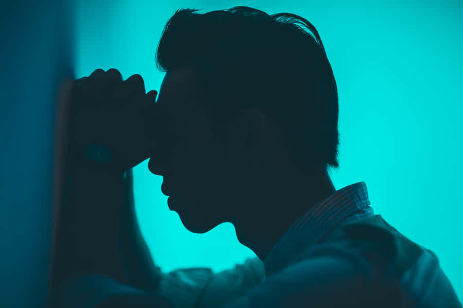 A Man Is Leaning Against A Wall With His Hand On His Face Wallpaper
