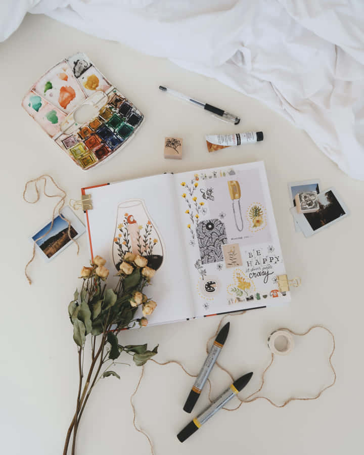 A Notebook, Flowers, And Other Items Are Laid Out On A Bed Wallpaper