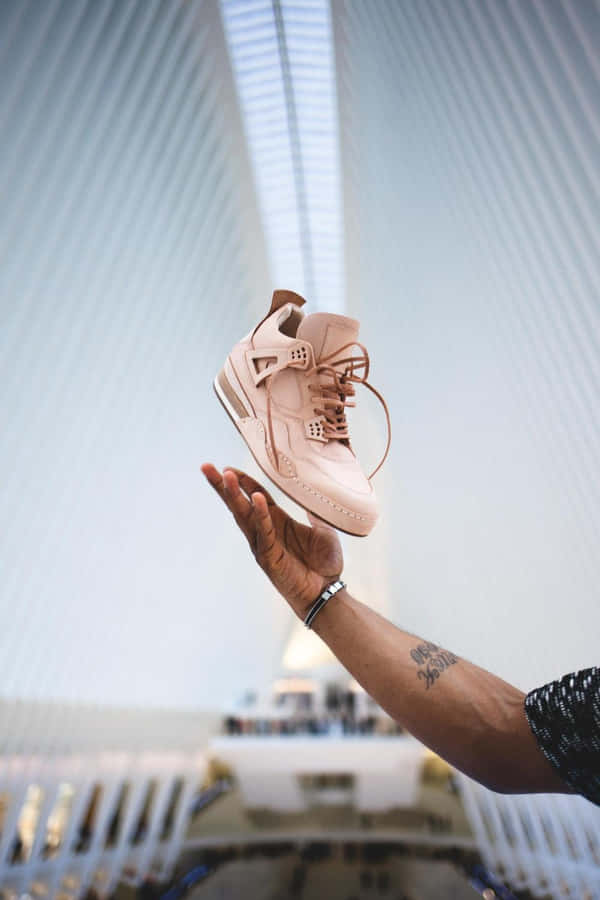 A Person Holding A Pink Shoe In Front Of A Building Wallpaper
