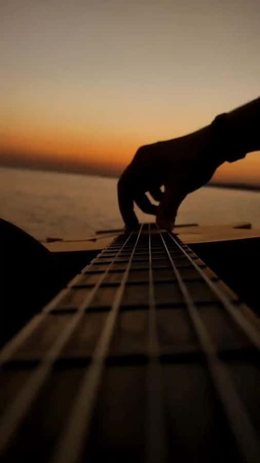 A Person Playing An Acoustic Guitar At Sunset Wallpaper