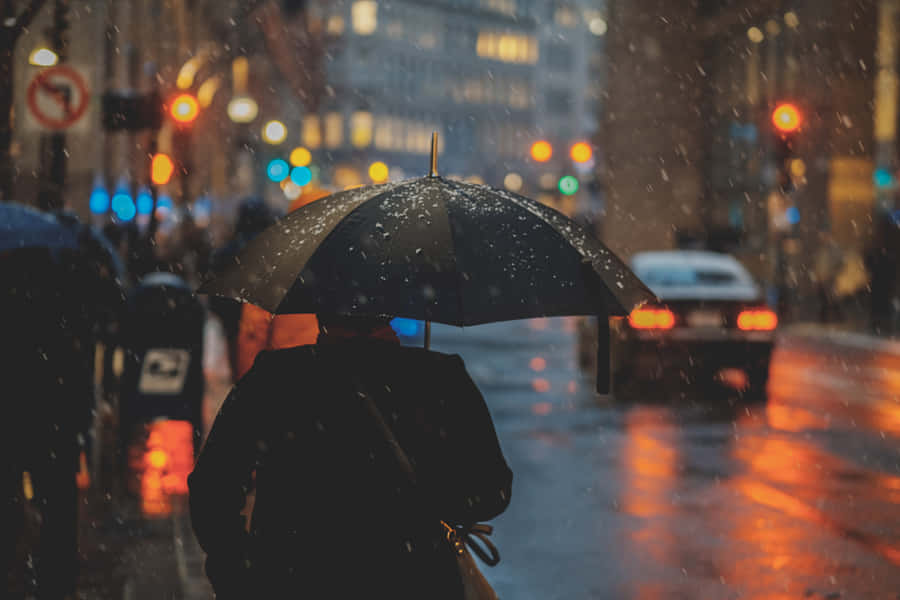 A Person Walking Down A City Street With An Umbrella Wallpaper