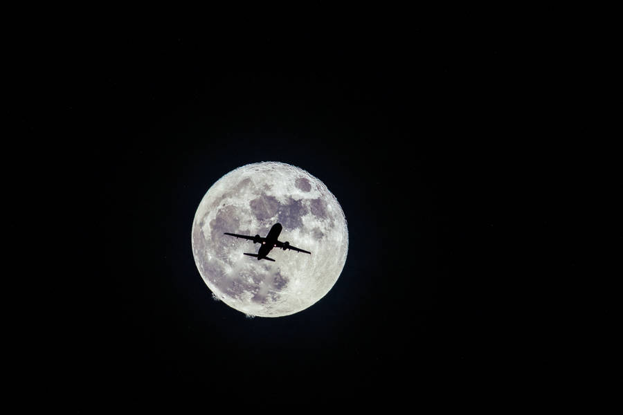 A Silhouetted Airplane Soaring Against A Nocturnal Starry Sky Wallpaper