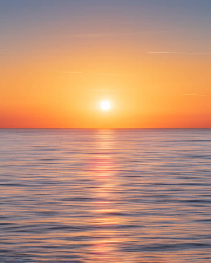 A Stunningly Beautiful Sunset Over The Calm And Inviting Ocean. Wallpaper
