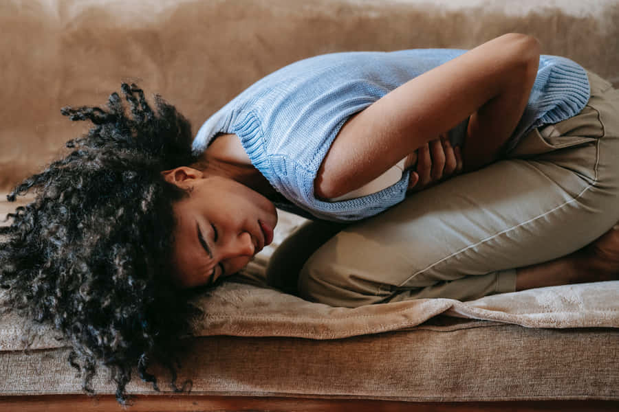 A Woman Is Lying On A Couch With Her Stomach Hurting Wallpaper