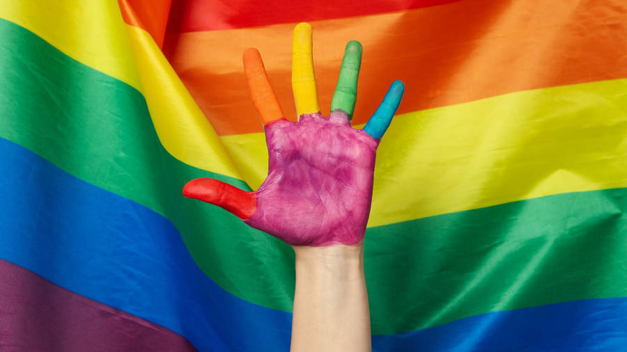 A Woman's Hand Painted With Rainbow Colors Is Raised Up Against A Rainbow Flag Wallpaper
