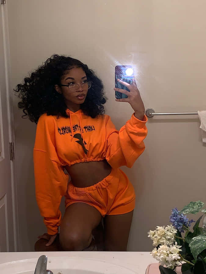 A Woman Taking A Selfie In An Orange Sweatsuit Wallpaper