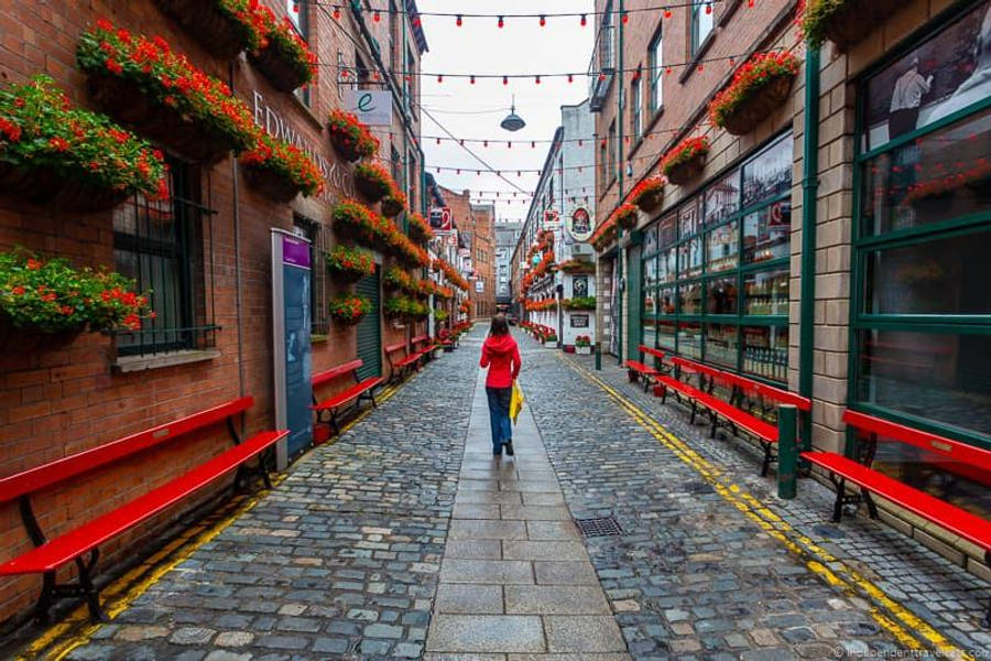 A Woman Walking Down A Narrow Street With Red Benches Wallpaper