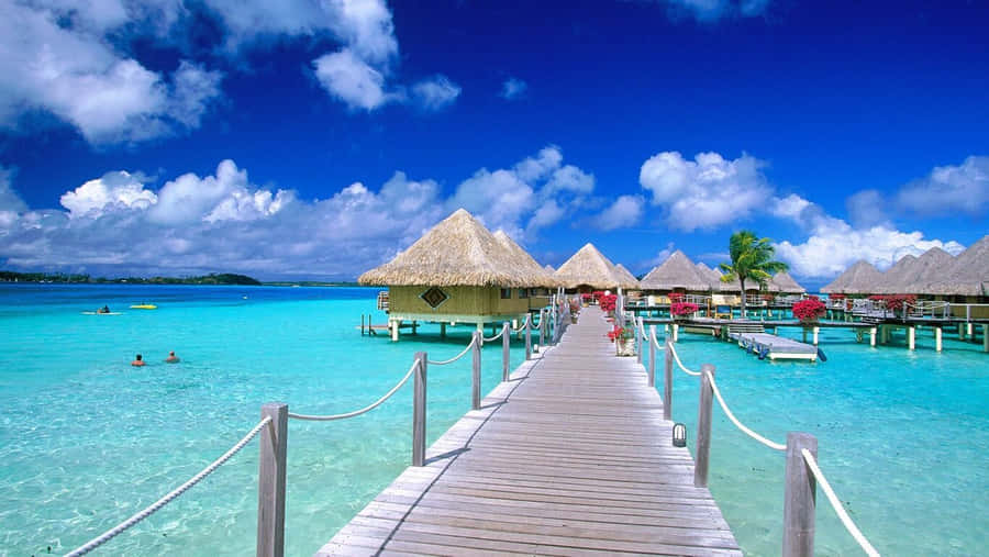 A Wooden Walkway Leading To A Beach With Huts Wallpaper