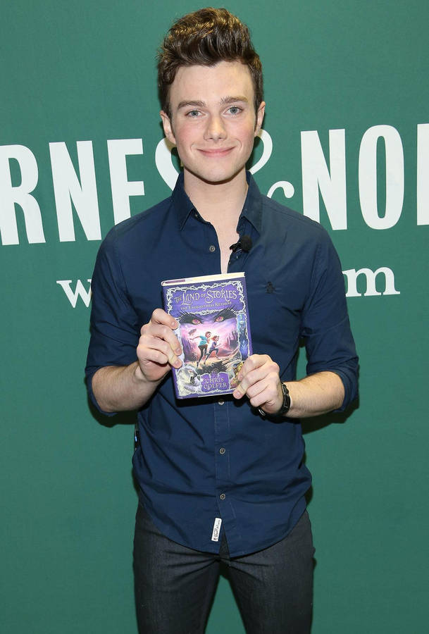 Award-winning Author Chris Colfer Posing With His Best-selling Book 'the Land Of Stories'. Wallpaper