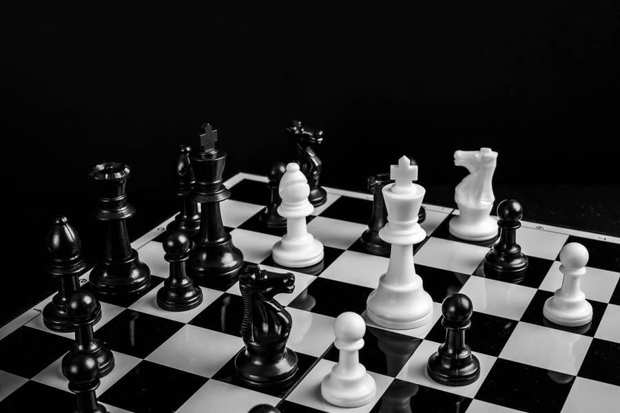 Caption: Engaging Mind Games: Black And White Plastic Chess Pieces On The Board Wallpaper