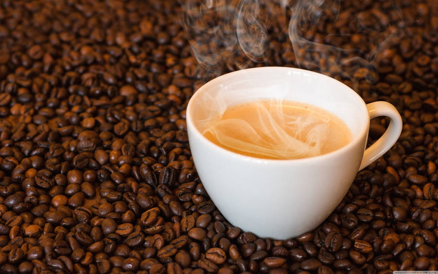 Caption: Invigorating Steaming Coffee Cup Resting On Raw Arabica Coffee Beans. Wallpaper