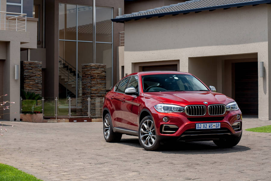 Caption: Luxurious Bmw X6 M Parked Outside A Modern House Wallpaper