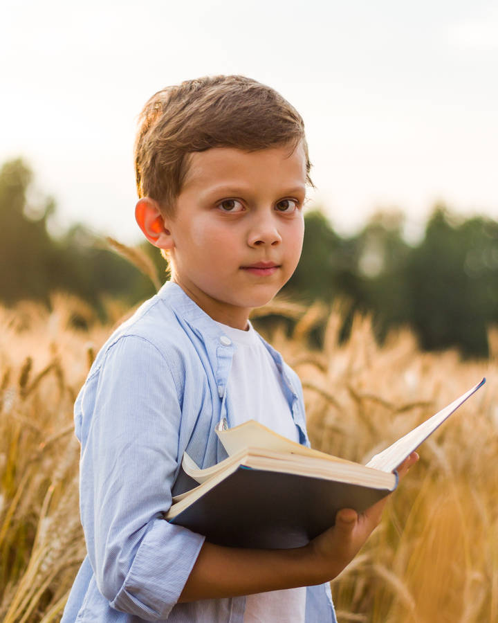 Cute Boy Standing With Open Book Wallpaper