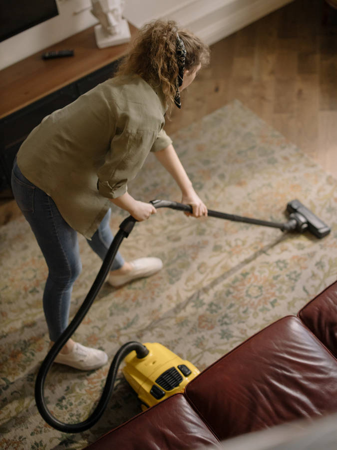 Dedicated Housekeeper Cleaning A Floor With A Vacuum Cleaner Wallpaper