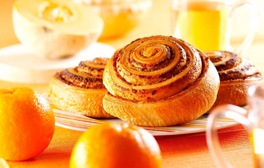 Delicious Cinnamon Rolls Served With Fresh Oranges Wallpaper