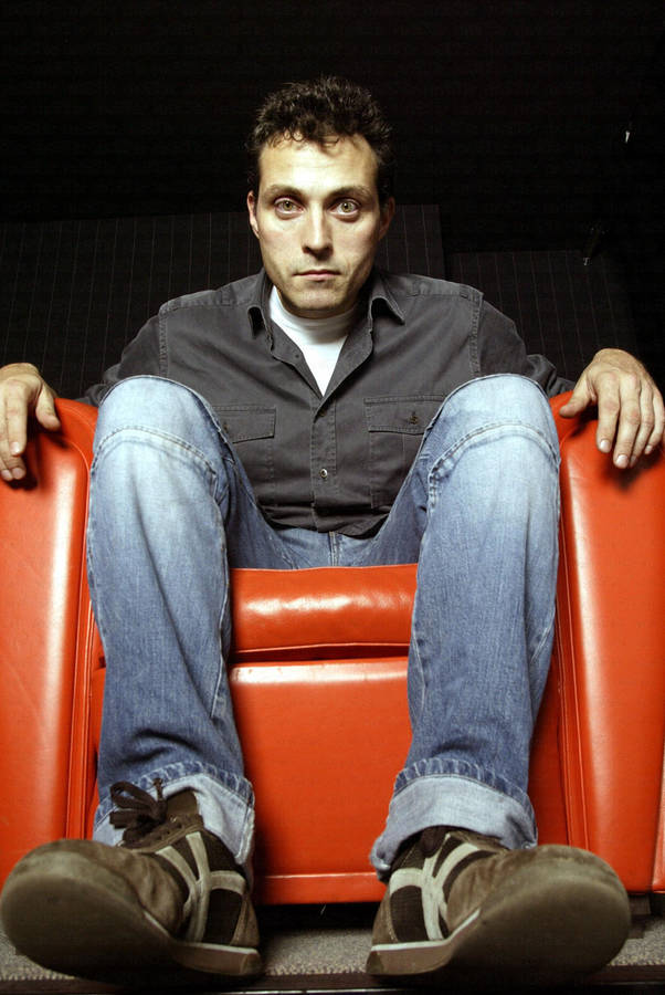 Eerie Rufus Sewell Sitting On An Orange Recliner Wallpaper