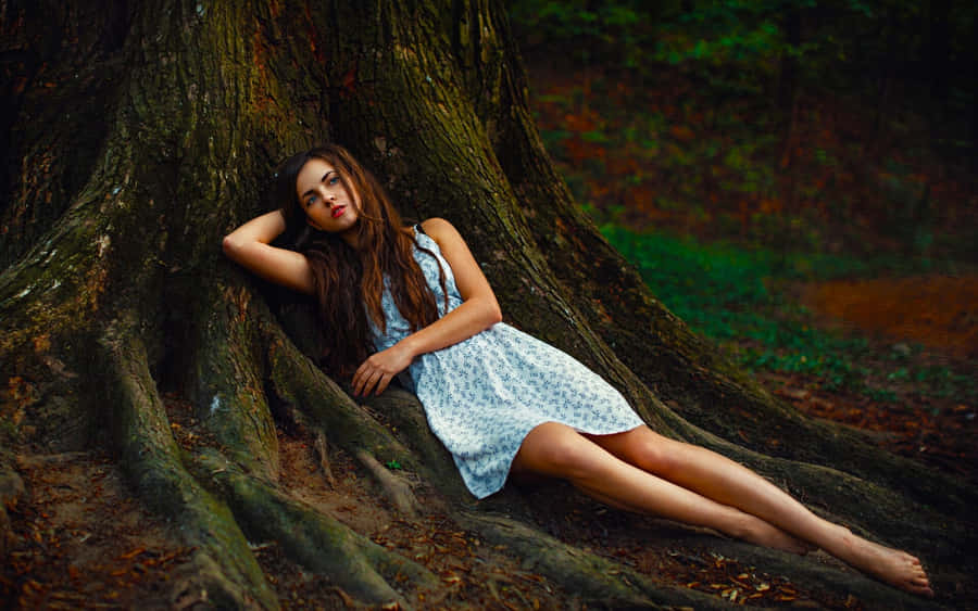 Elegant_ Woman_ Reposing_ Against_ Tree_ Roots Wallpaper