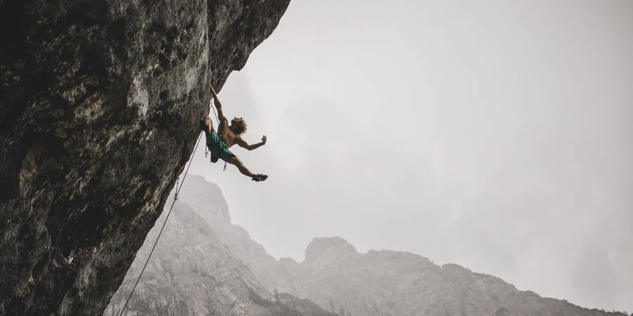 Fearless Adventurer Conquers The Cliff Amidst Stormy Skies Wallpaper