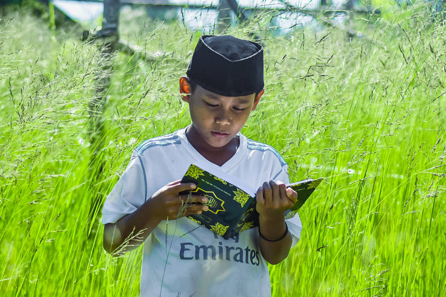 Islamic Boy Reading Quran Outdoors Wallpaper