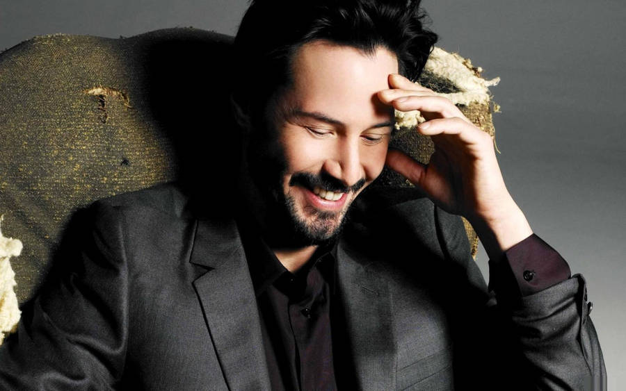 Keanu Reeves Laughing In Chair Wallpaper