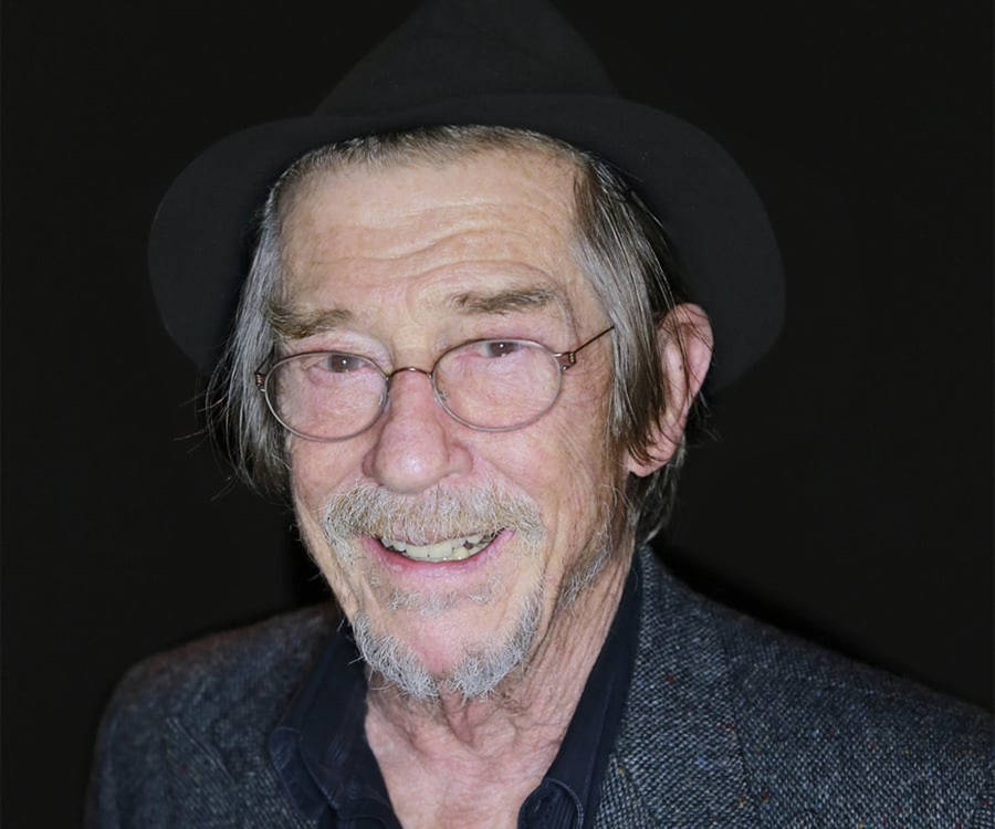 Legendary Actor John Hurt In Hat And Glasses Against A Black Background Wallpaper