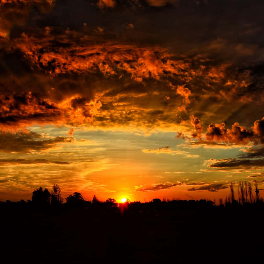Majestic Orange Sunset Behind Dusky Clouds Wallpaper