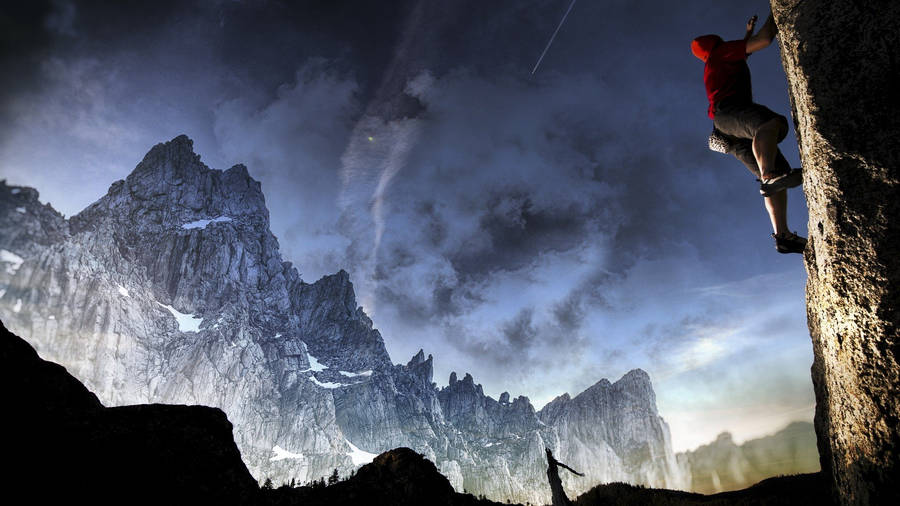 Man Climbing A Rock Overlooking Icy Mountains Wallpaper