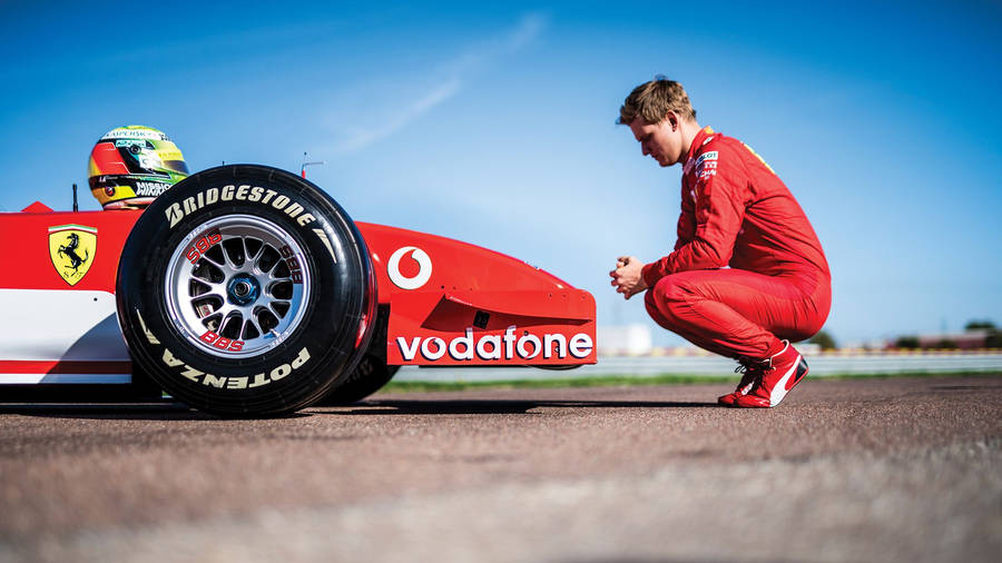 Mick Schumacher Crouching Beside A Car Wallpaper