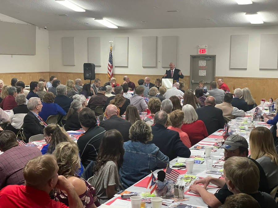 Mike Gibbons Delivering Speech In Packed Room Wallpaper