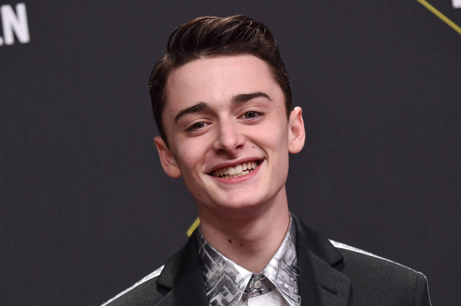 Noah Schnapp Smiling Against Dark Backdrop Wallpaper