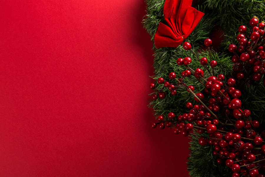 Perfect For The Holiday Season: A Red Christmas Wreath Set Against A White Wall Wallpaper
