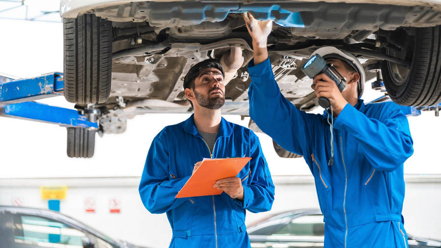 Proficient Mechanical Engineer Technician Inspecting A Car Wallpaper