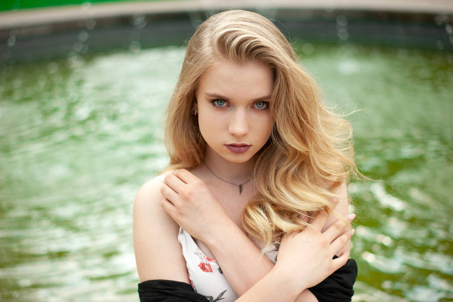 Serene Blonde Woman Enjoying A Moment By The Fountain Wallpaper