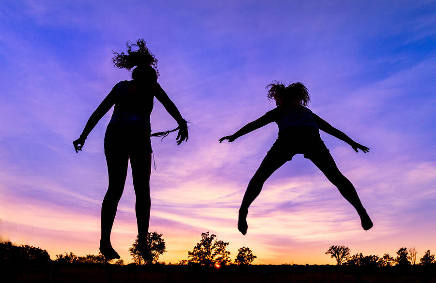 Silhouetted Girls Jumping From A Trampoline Wallpaper